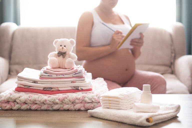 valise maternité une femme enceinte assise sur un canapé avec un carnet a la main et elle écrit une liste de valise de maternité